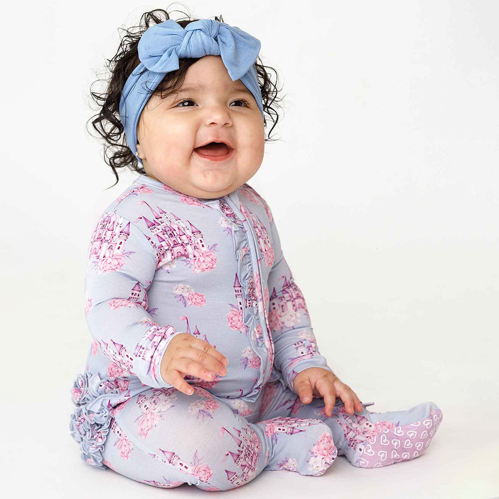 Baby wearing a floral onesie and blue headband on a white background