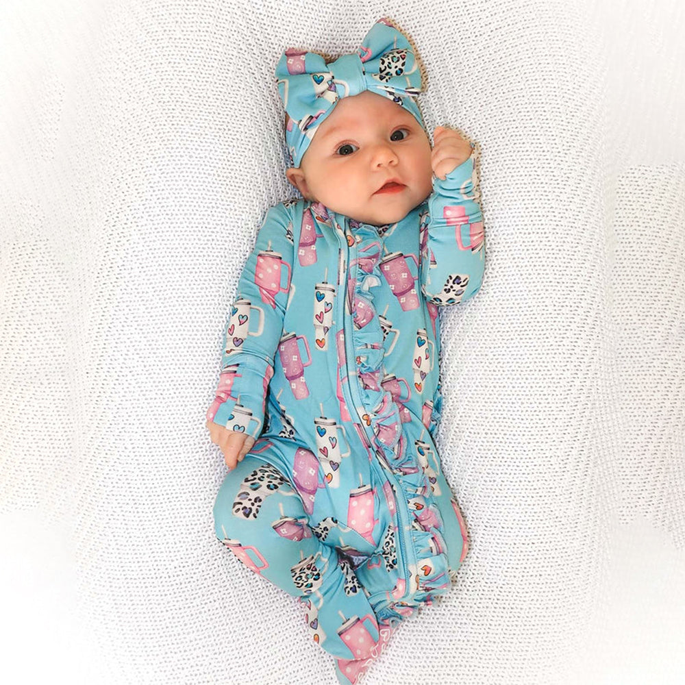 Baby in a blue and pink patterned outfit with a matching headband on a textured white background