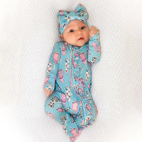 Baby in a blue and pink patterned outfit with a matching headband on a textured white background
