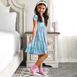 Child wearing a blue dress with pink and white cup print, holding a matching pink tumbler.