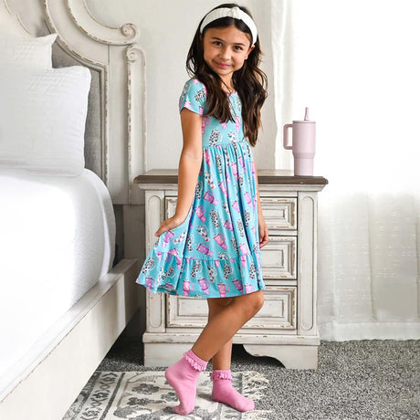 Child wearing a blue dress with pink and white cup print, holding a matching pink tumbler.