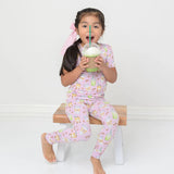 Child in pink pajama set with cartoon design, holding a green drink with a straw.