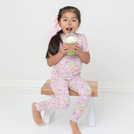 Child in pink pajama set with cartoon design, holding a green drink with a straw.