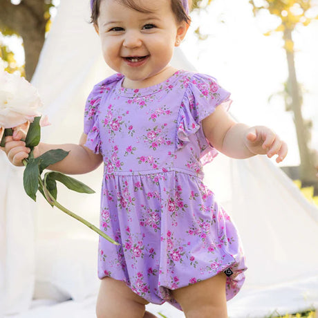 Baby in a purple floral dress holding flowers outdoors