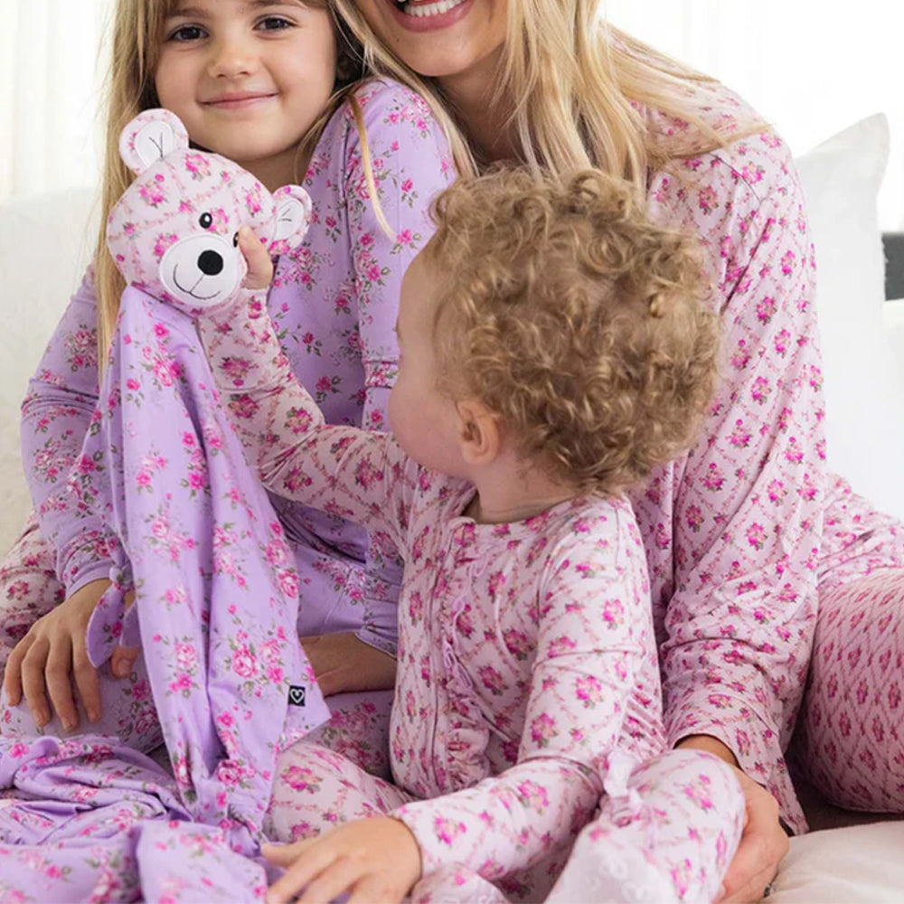 Woman and two children in matching floral pajamas with a teddy bear.