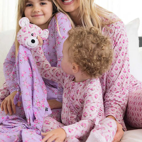Woman and two children in matching floral pajamas with a teddy bear.