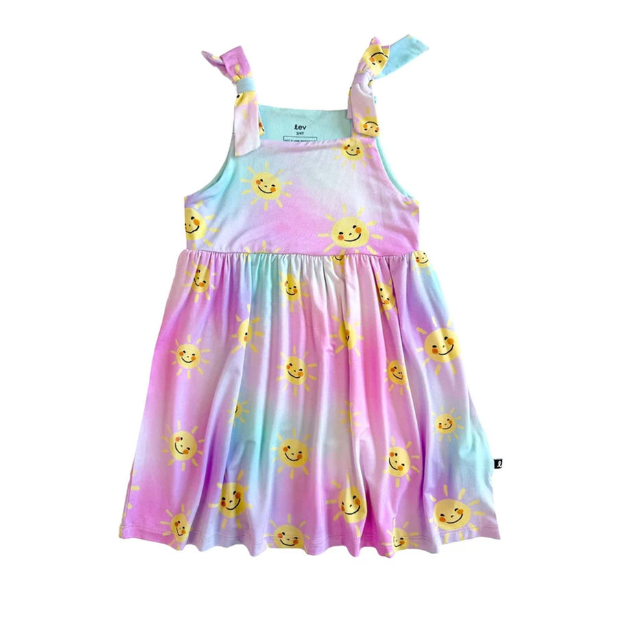 a children's dress with a pastel tie-dye gradient in pink, blue, and purple, featuring a yellow smiley sun print and a knotted shoulder strap, shown on a white background.