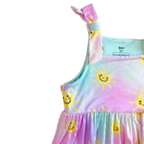 Close-up of a children's dress with a pastel tie-dye gradient in pink, blue, and purple, featuring a yellow smiley sun print and a knotted shoulder strap, shown on a white background.