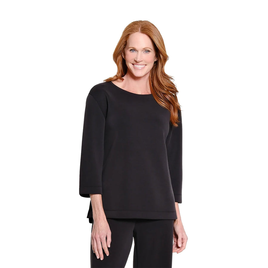 A smiling woman with long red hair wearing a black three-quarter sleeve top and black pants, standing against a plain white studio background.