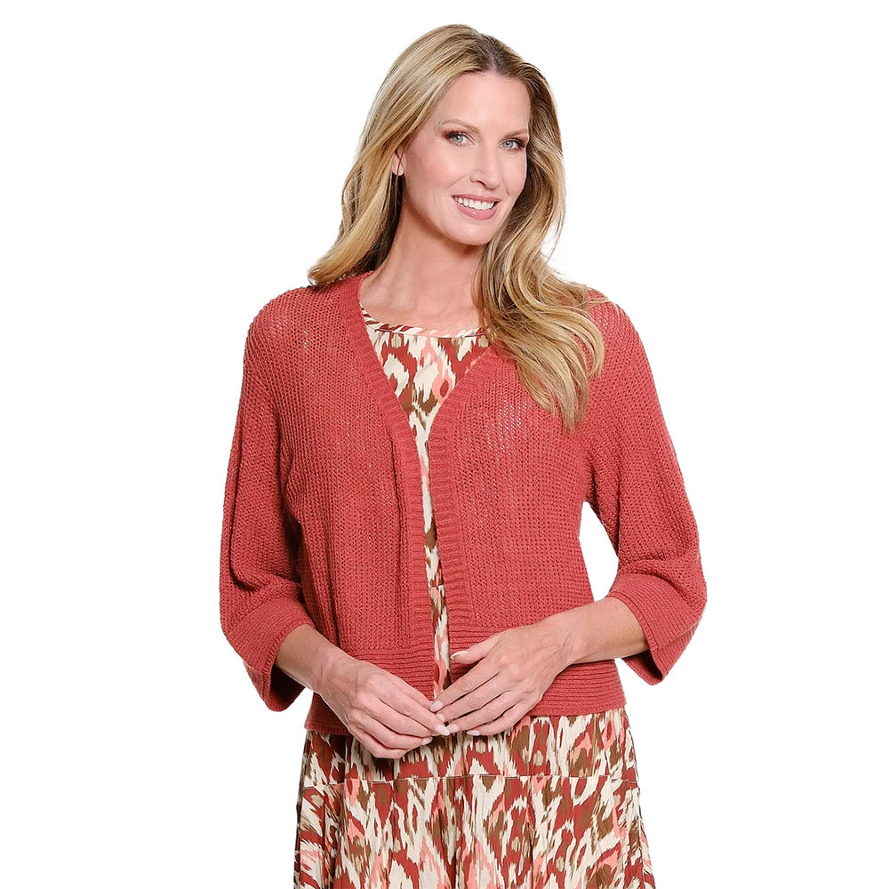 A woman modeling a rust-colored knit cardigan over a patterned midi dress with a matching headband, paired with strappy high-heeled sandals, against a plain white background.