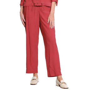 A model is wearing a pair of wide-leg cropped trousers in a dusty rose red color, paired with a matching top and cream-colored loafers, shown against a plain white background.