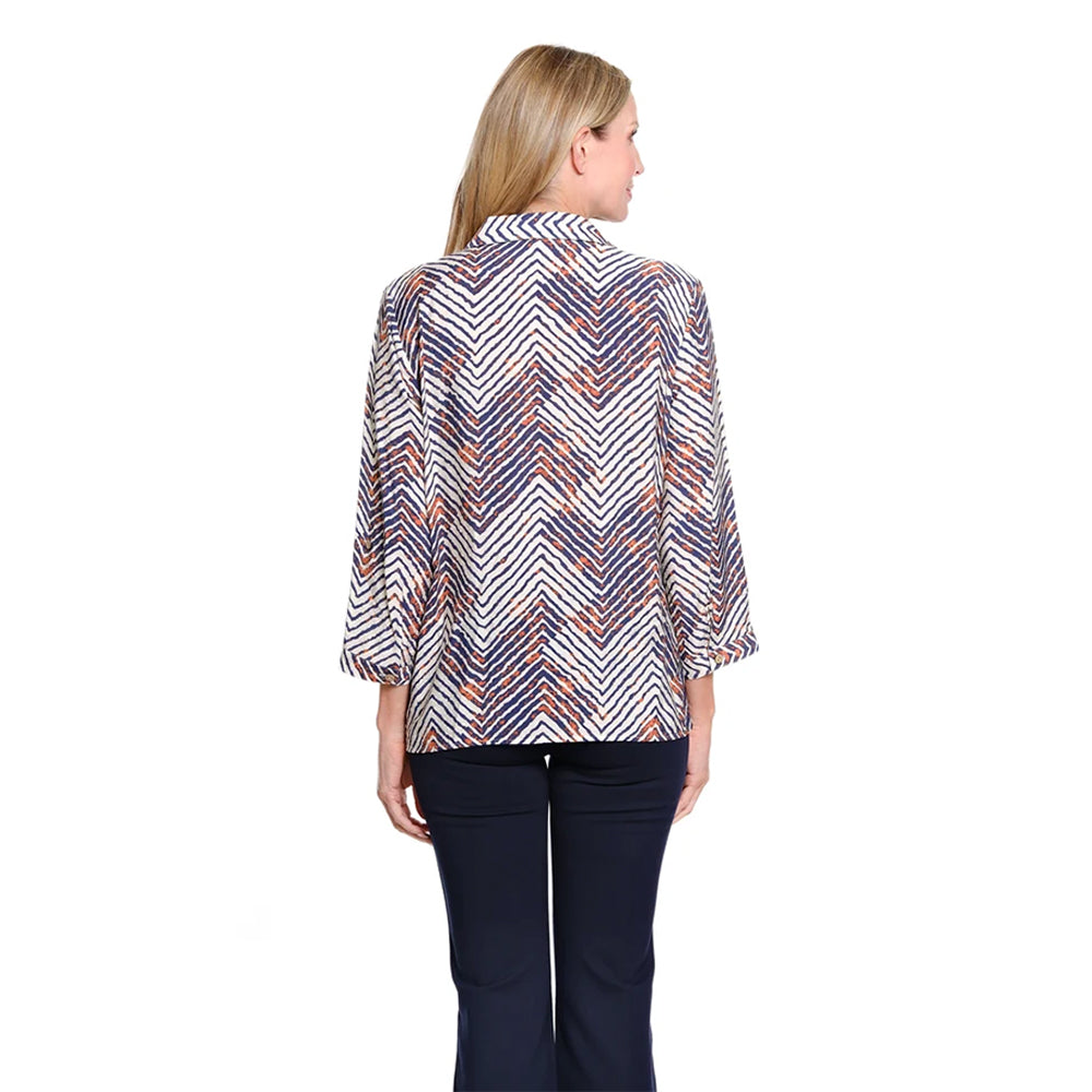 A woman viewed from the back wearing a long-sleeve collared blouse with a white, navy, and orange chevron pattern, paired with dark navy pants, against a plain white background.