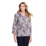 A woman modeling a long-sleeve button-up blouse with a geometric chevron pattern in navy blue, orange, and white, paired with dark navy pants, against a solid white background.