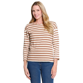 A woman modeling a long-sleeve boat-neck top with horizontal tan and off-white stripes, paired with blue jeans, against a plain white background.