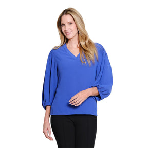 A woman modeling a royal blue blouse with a V-neckline and voluminous elbow-length sleeves, paired with black pants, against a plain white background.