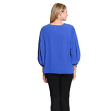 A woman viewed from the back wearing a royal blue long-sleeve blouse with balloon sleeves and black pants, set against a plain white background.