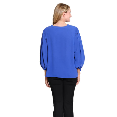 A woman viewed from the back wearing a royal blue long-sleeve blouse with balloon sleeves and black pants, set against a plain white background.