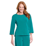 A smiling woman with long red hair wearing a teal green three-quarter sleeve top and matching pants, photographed against a plain white background.