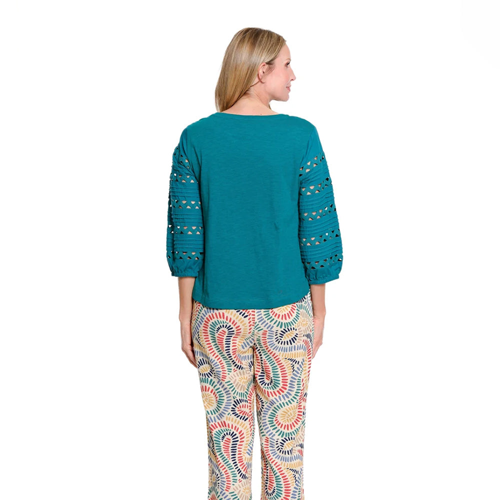 A woman shown from the back wearing a teal long-sleeve top with crochet sleeve details and patterned pants with a multicolor paisley design, set against a plain white background.