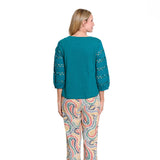 A woman shown from the back wearing a teal long-sleeve top with crochet sleeve details and patterned pants with a multicolor paisley design, set against a plain white background.
