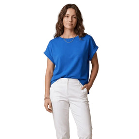 Woman wearing a blue shirt and white pants against a beige background