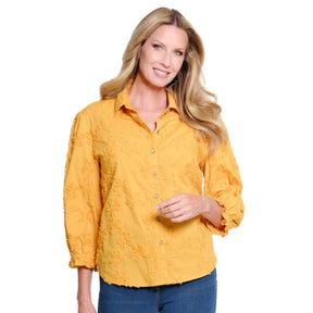 A woman modeling a mustard yellow textured button-up blouse with three-quarter sleeves, paired with blue jeans, against a plain white background.