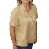 Woman wearing a beige blouse with button details against a stone wall.