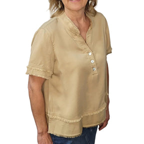 Woman wearing a beige blouse with button details against a stone wall.