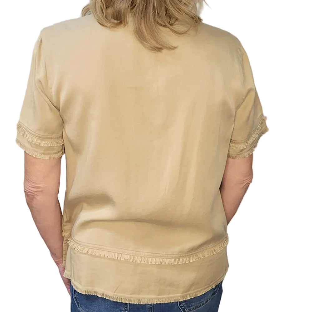 Person wearing a beige blouse with lace trim in front of a gray brick wall.