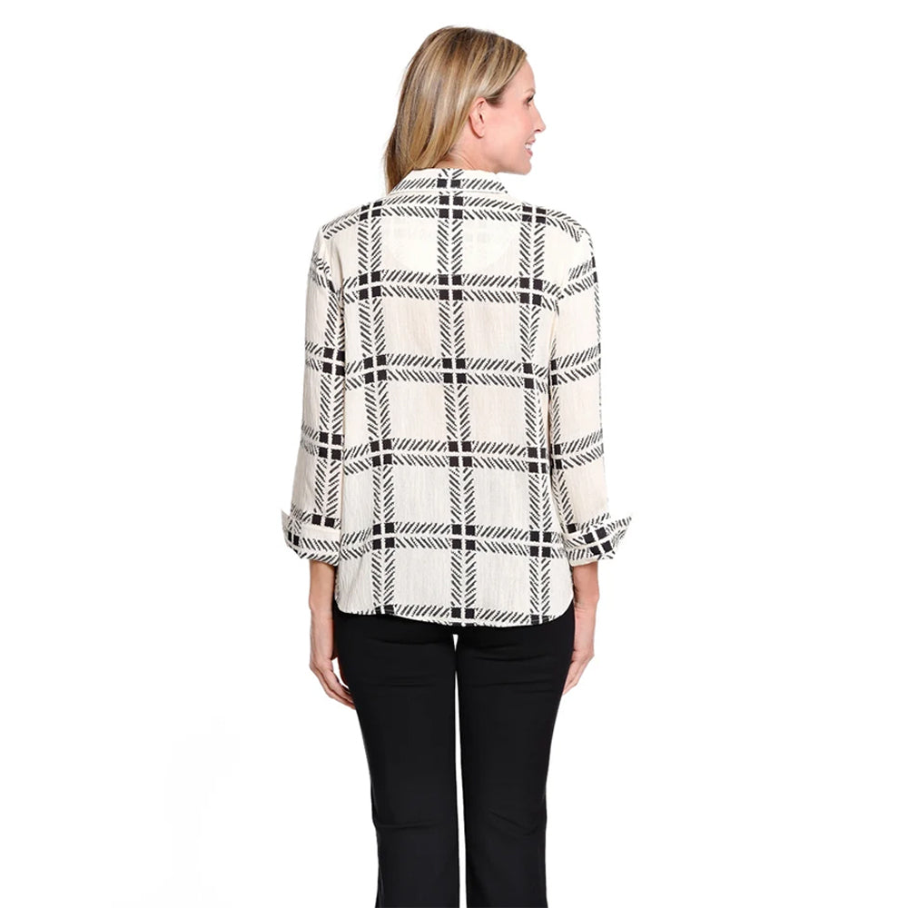 A woman viewed from the back wearing a cream-colored long-sleeve blouse with a black plaid pattern and black pants, set against a plain white background.