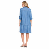 A woman viewed from the back wearing a light blue tiered shirt dress with three-quarter sleeves, shown against a plain white background.