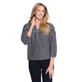 A woman modeling a navy and white vertically striped long-sleeve blouse with a buttoned split neckline, paired with dark pants, against a plain white background.