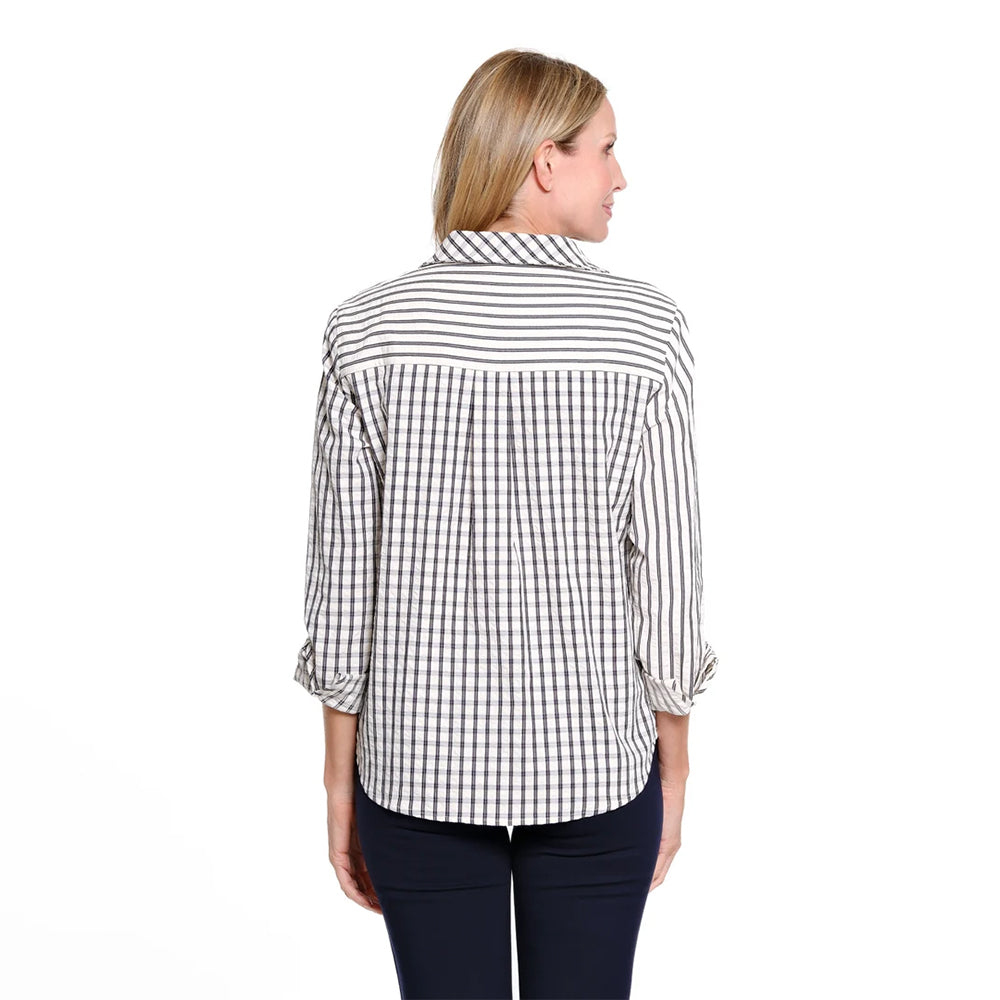 A woman viewed from the back wearing a white button-up shirt with black vertical and small check stripes, paired with dark navy pants, against a plain white background.