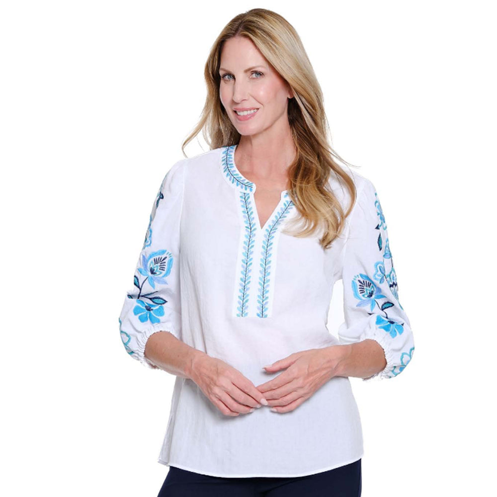 Woman wearing a white blouse with blue floral embroidery on a white background