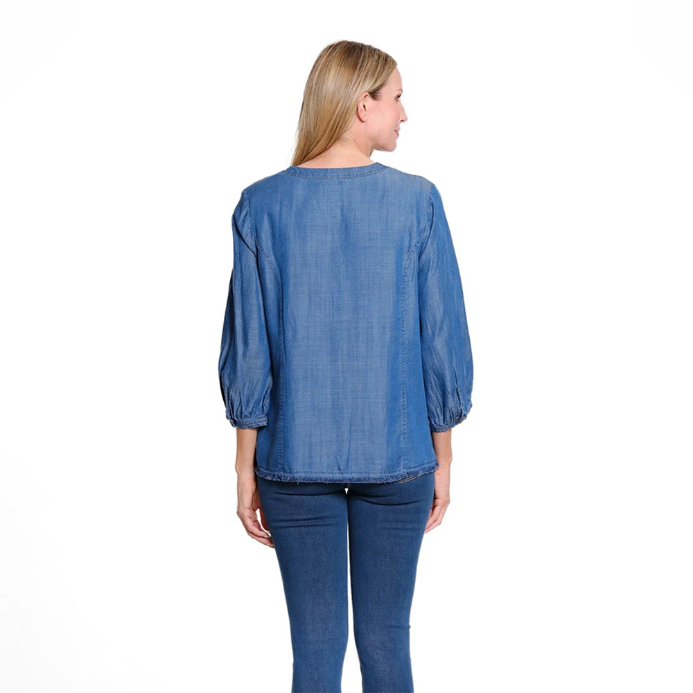 A woman viewed from the back wearing a blue long-sleeve blouse with gathered cuffs and dark blue jeans, photographed against a plain white studio background.