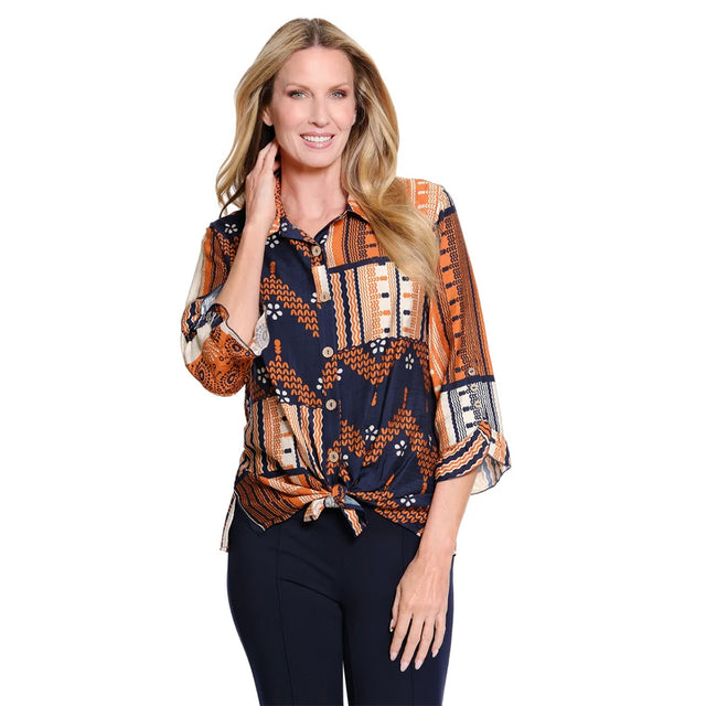 A woman modeling a patterned button-up blouse with three-quarter sleeves and a tied waist, paired with dark pants, against a plain white background.