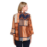 A woman shown from the back wearing a patchwork-style blouse with orange, navy, beige, and white geometric and floral patterns, paired with dark navy pants, against a plain white background.