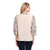A woman shown from the back wearing a beige blouse with patterned three-quarter sleeves and dark navy pants, photographed against a plain white studio background.