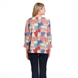 A woman viewed from the back wearing a long-sleeve blouse with a geometric patchwork pattern in beige, red, and blue, paired with dark navy pants, against a plain white background.