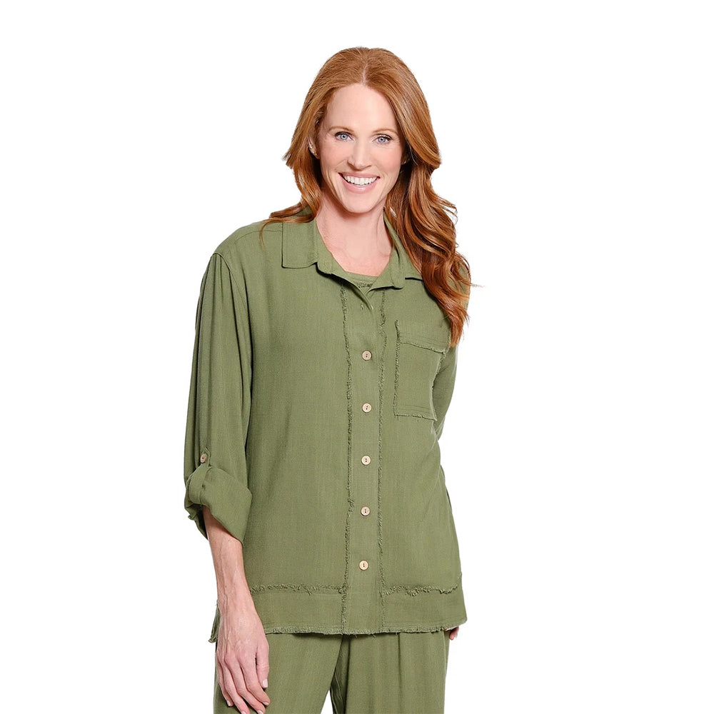 A smiling woman with long red hair wearing an olive green button-up shirt and matching green pants, photographed against a plain white studio background.
