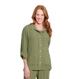 A smiling woman with long red hair wearing an olive green button-up shirt and matching green pants, photographed against a plain white studio background.