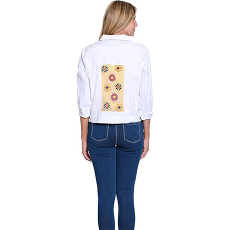 Woman wearing a white shirt with a colorful floral design on the back, standing against a white background.