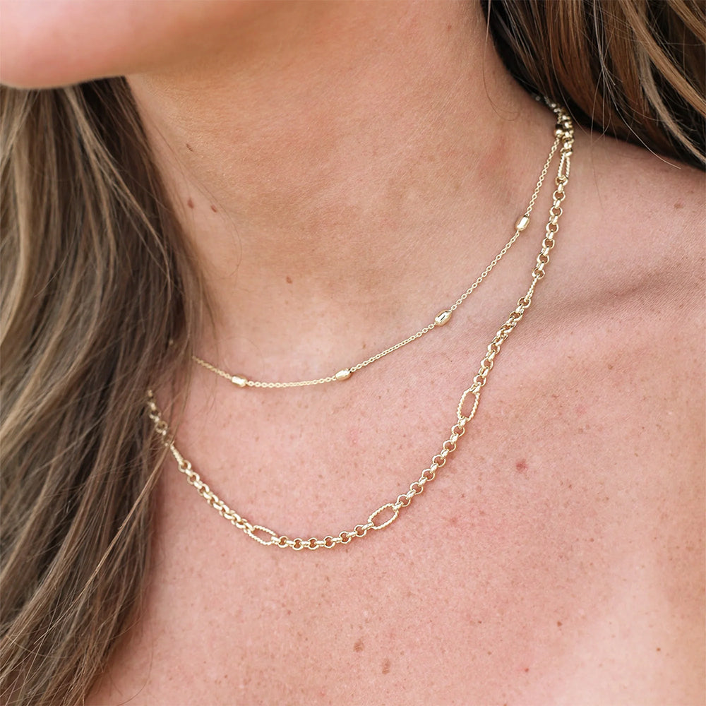 Close-up of a person wearing two gold necklaces on a plain background