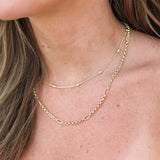 Close-up of a person wearing two gold necklaces on a plain background