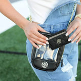 Person holding a clear crossbody bag with a black wallet against a grassy background