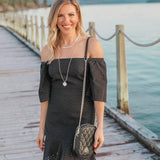 Woman in a black dress with a quilted handbag standing on a wooden dock by a body of water.
