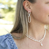 Close-up of a person wearing a silver earring and pearl necklace outdoors.