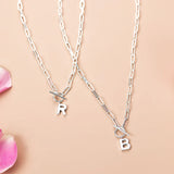 Two silver necklaces with letter charms on a beige background
