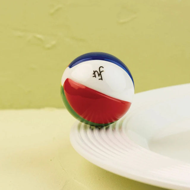 A small decorative ball with blue, white, red, and green sections sits on the edge of a white plate against a pale yellow-green textured background.