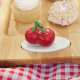 Decorative red cherry on a white base with a wooden surface and checkered tablecloth in the background.
